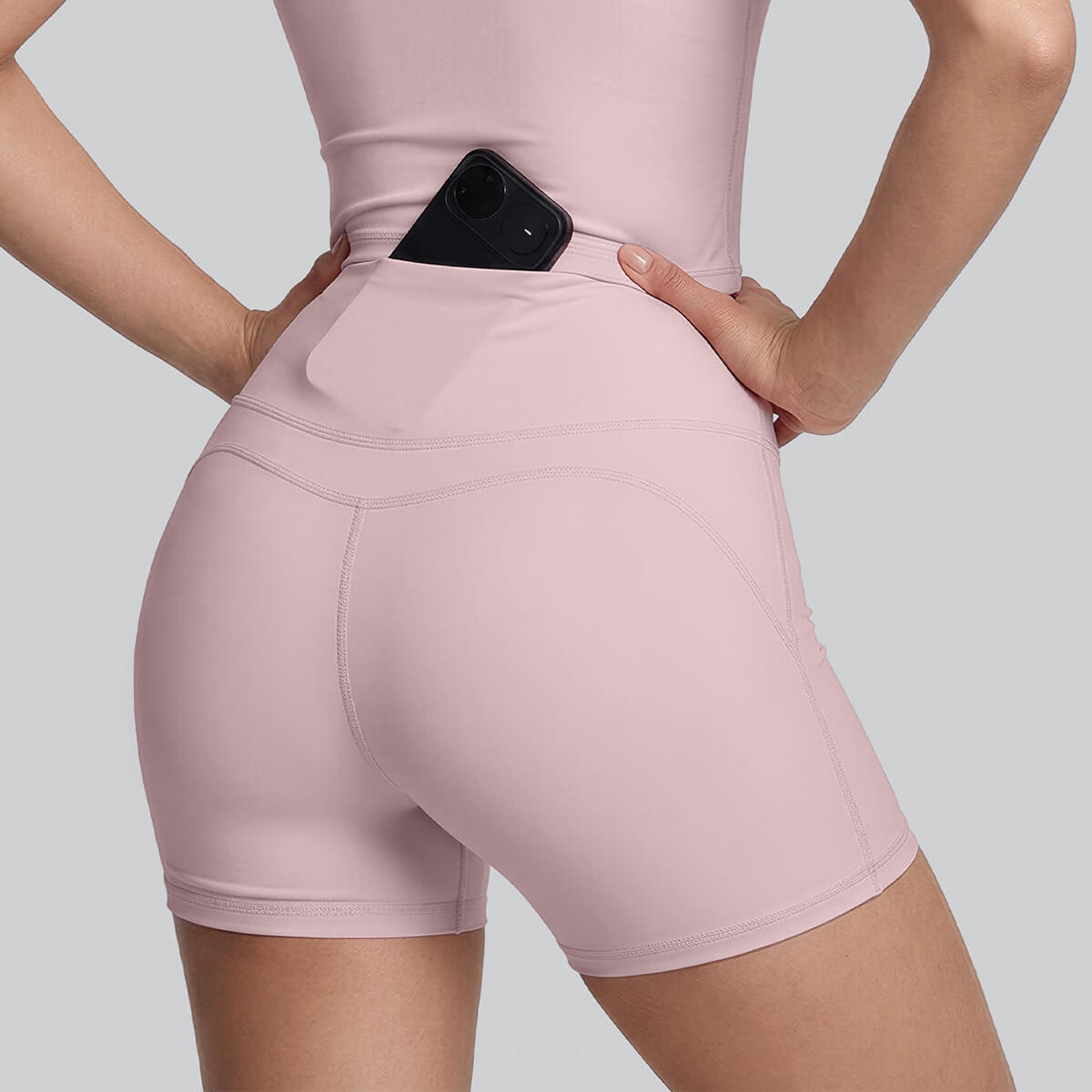 Back view of women's pink high-waisted yoga shorts featuring a hidden waistband pocket with a smartphone inside