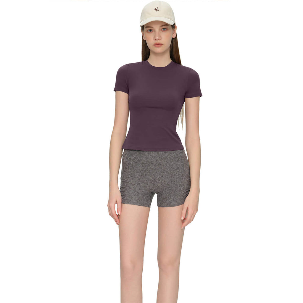 A woman wearing a plum purple athletic t-shirt paired with gray heathered workout shorts for an active lifestyle.