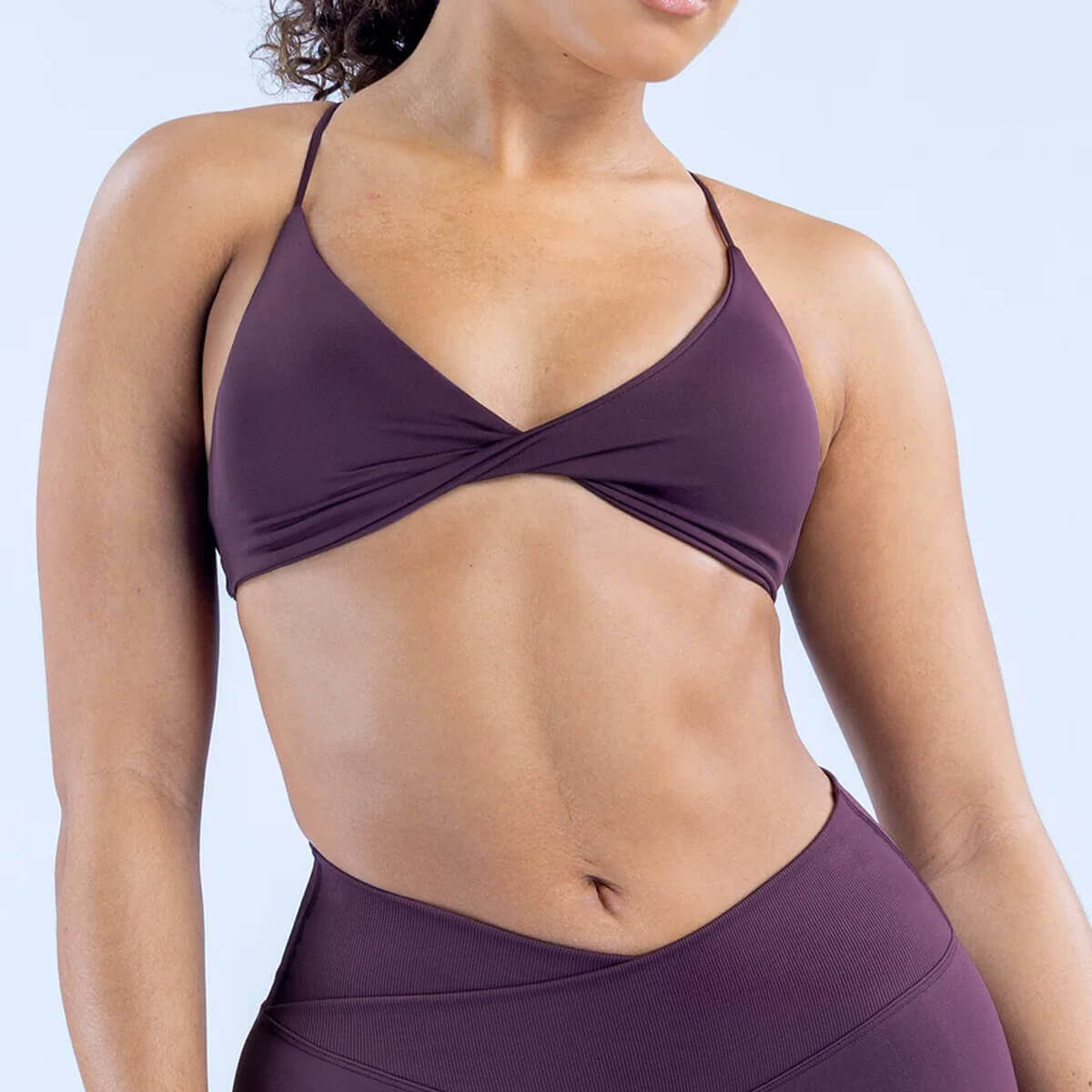 Front view of a plum purple athletic bralette with a chic center twist and matching v-cut leggings.