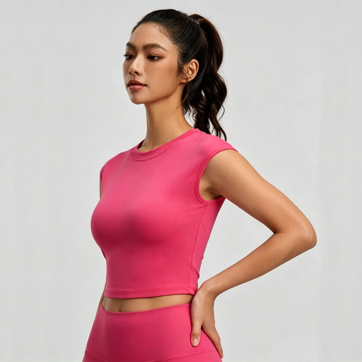 Side view of a vibrant fuchsia pink athletic crop top with a high neckline and cap sleeve silhouette, showcasing a minimalist vintage fitness aesthetic.