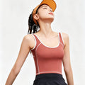 A woman wearing a rust red yoga crop top with white contrast piping and an orange sun visor, designed for outdoor tennis or running