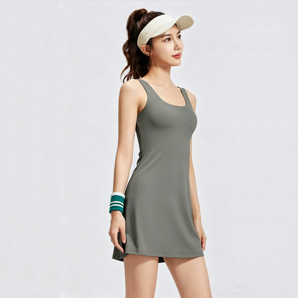 Front view of a woman wearing a sage green athletic tennis dress with a scoop neck and sleeveless A-line silhouette