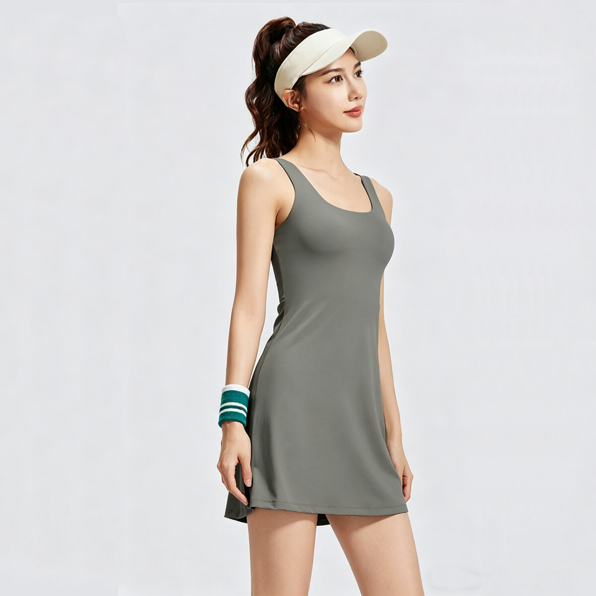 Front view of a woman wearing a sage green athletic tennis dress with a scoop neck and sleeveless A-line silhouette