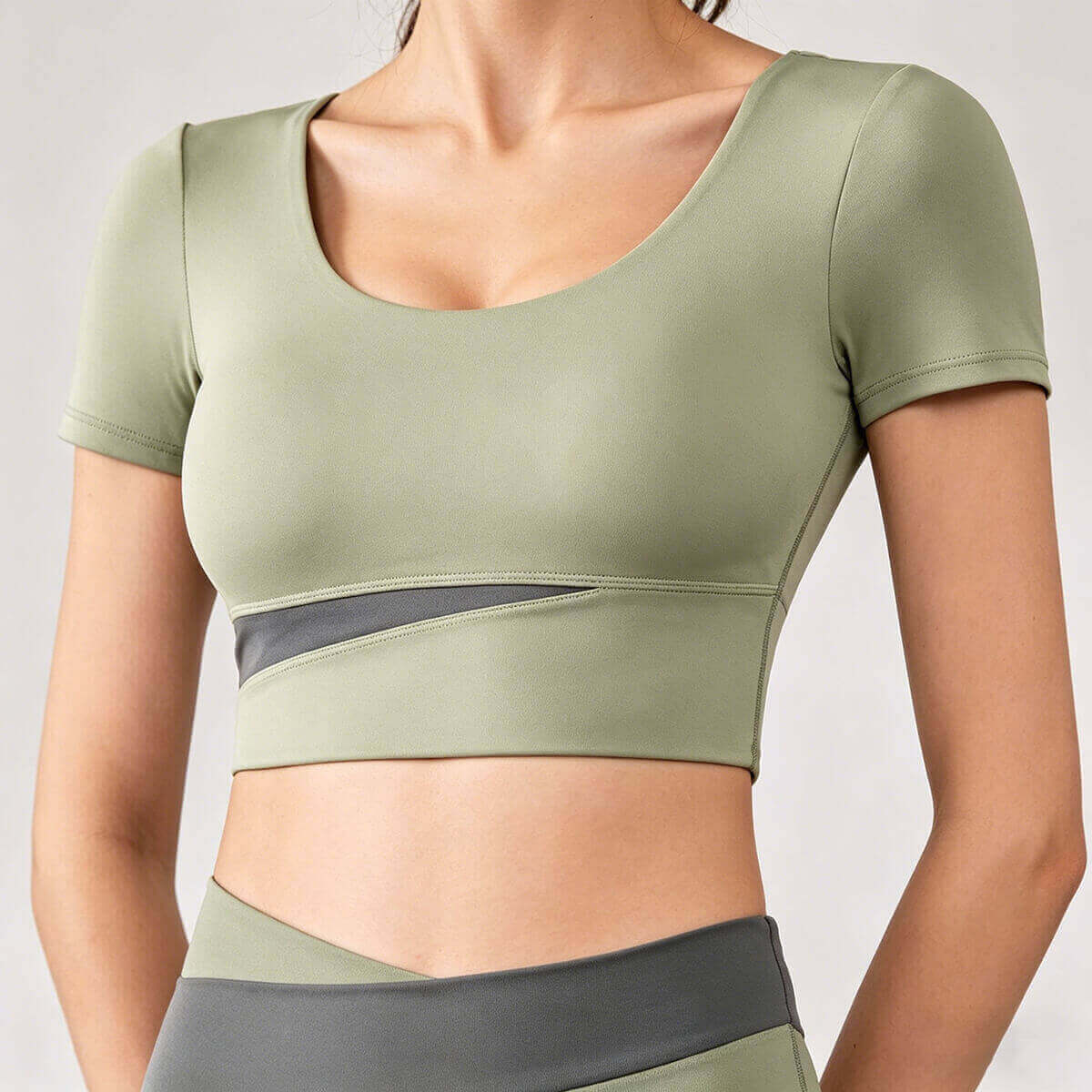Sage green performance workout crop top for women with a dark grey mesh accent, designed for moisture-wicking comfort and style.