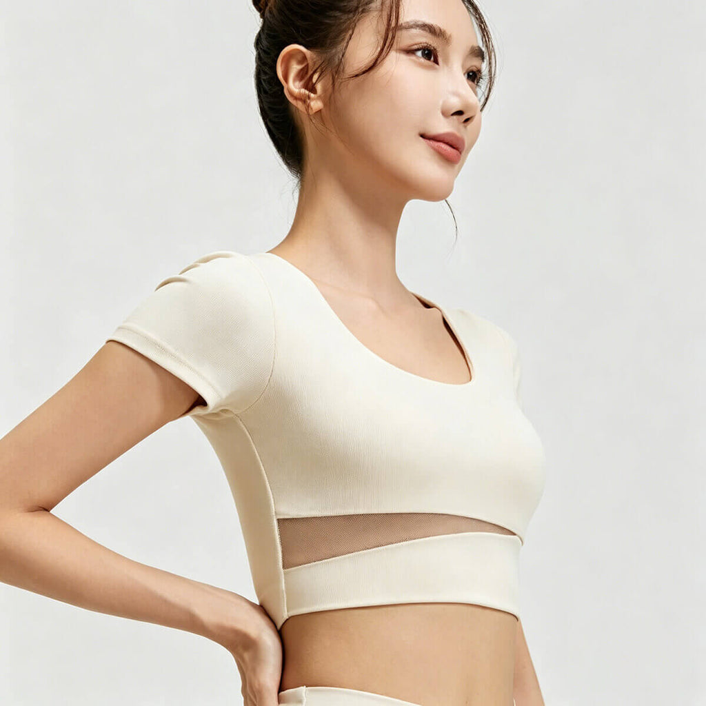 Side profile of a slim-fit ivory athletic crop top showing the breathable fabric and unique waist-slimming mesh panel design