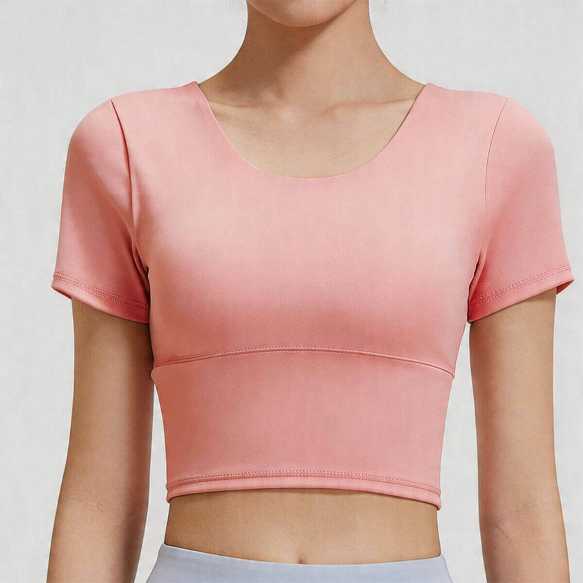 Front close-up of a scoop neck women's workout crop top in peach pink, featuring high-stretch fabric and a supportive wide band.