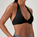 Side profile of a woman wearing a sleek black halter neck sports bra, showcasing the twist front detail and the comfortable open back design for athletic workouts.