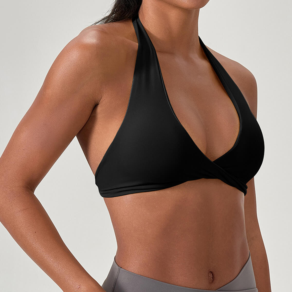 Side profile of a woman wearing a sleek black halter neck sports bra, showcasing the twist front detail and the comfortable open back design for athletic workouts.