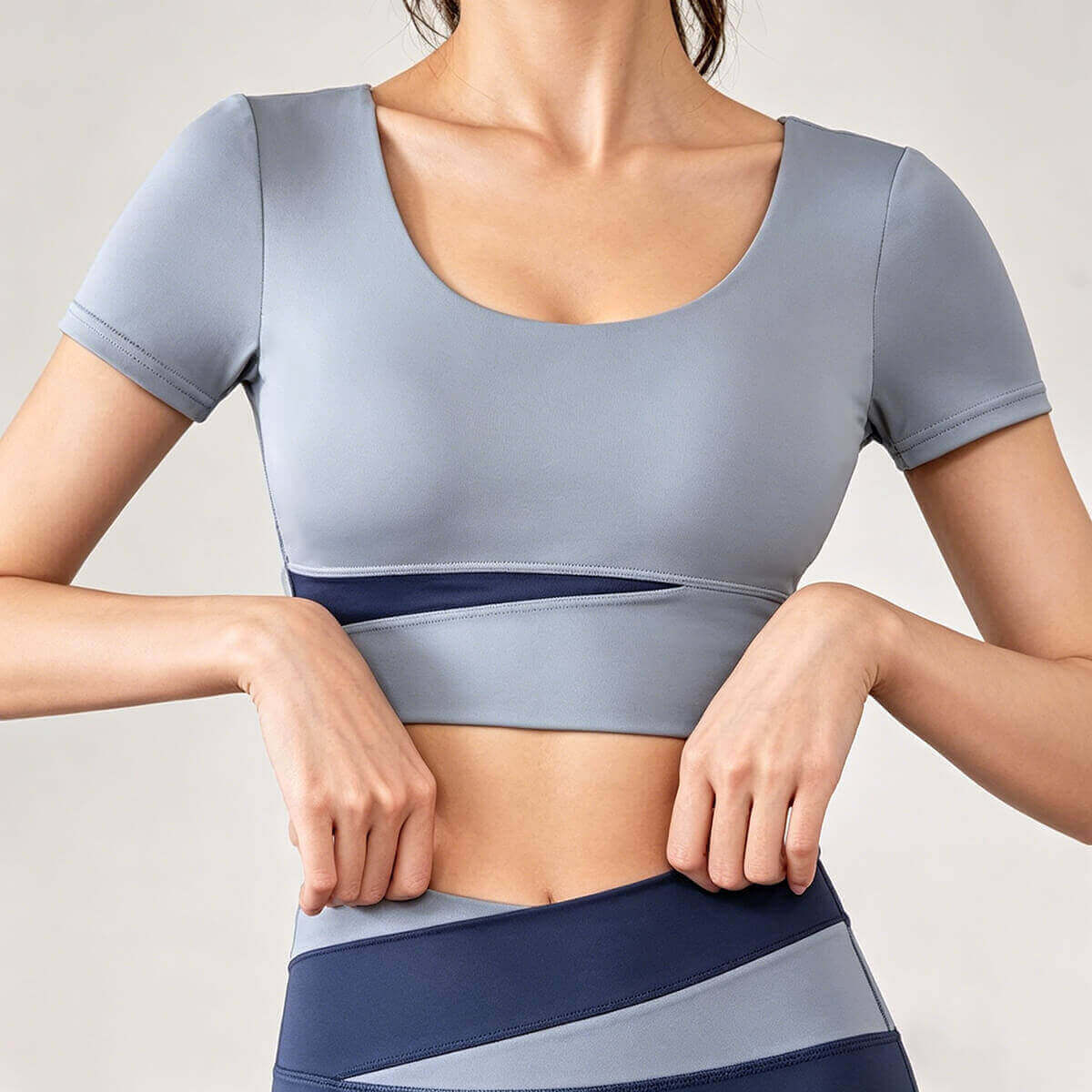 Women's slate blue short sleeve athletic top with a dark navy contrast mesh panel at the waist for enhanced ventilation during training.