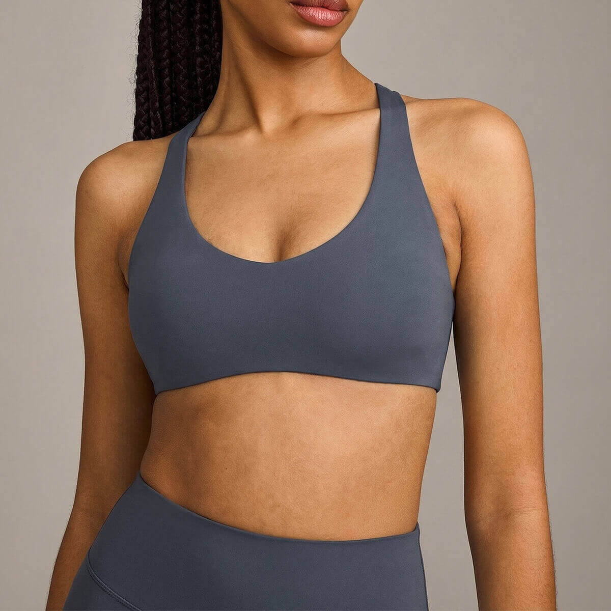 A woman with braids wearing a slate gray soft-fabric sports bra, showcasing a stylish and functional gym look.
