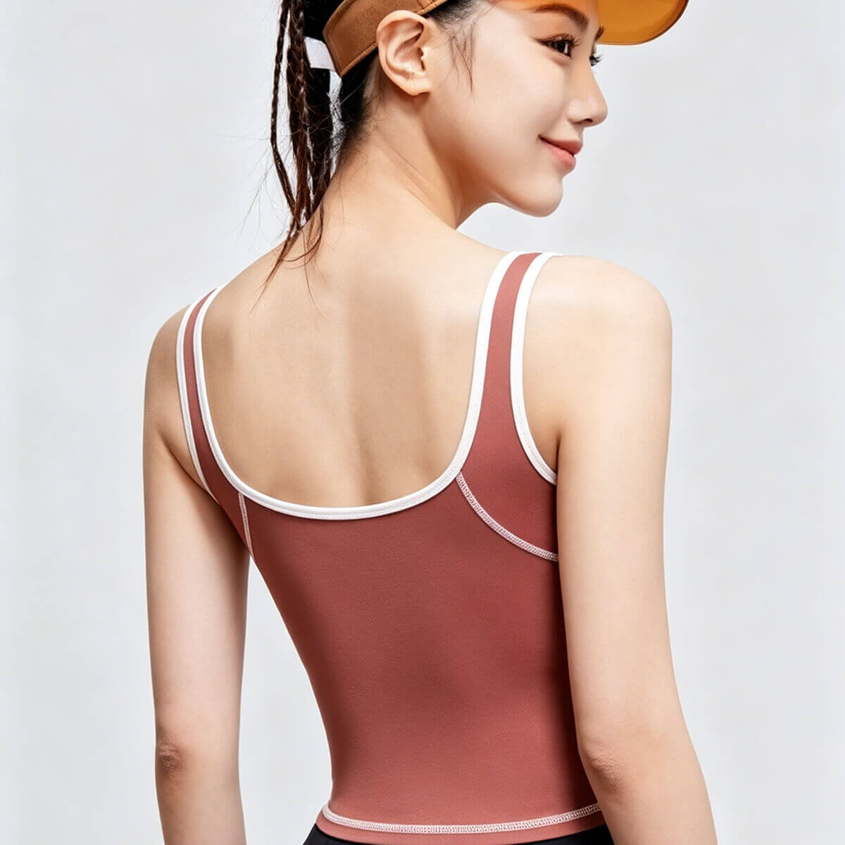 Side and back view of a rust-colored sports camisole featuring a scoop neck and deep U-back design with white trim