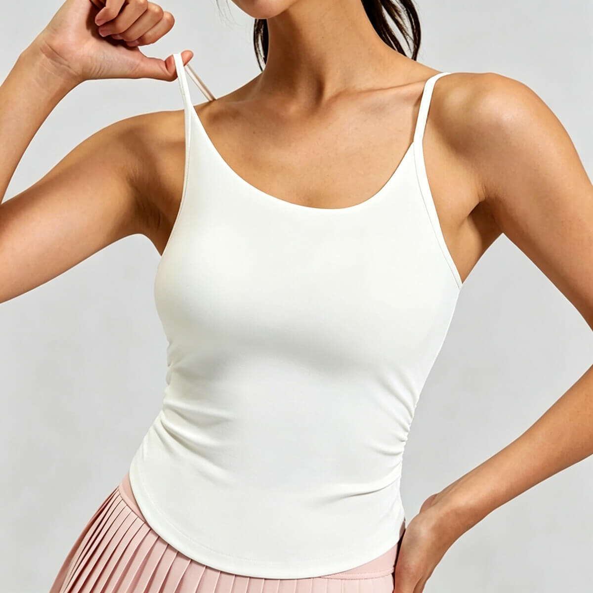 Front view of a white athletic tank top with a built-in shelf bra and thin spaghetti straps, featuring side ruching for a slimming fit