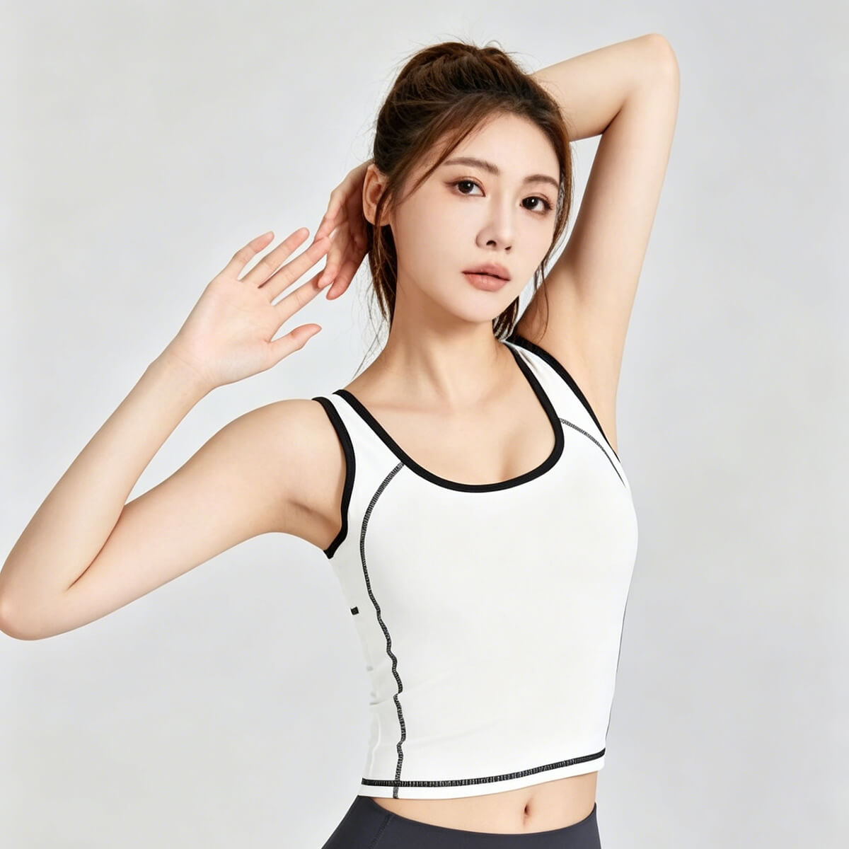 A white sleeveless yoga crop top with black contrast borders and stitching, modeled in a fitness pose for pilates or gym training