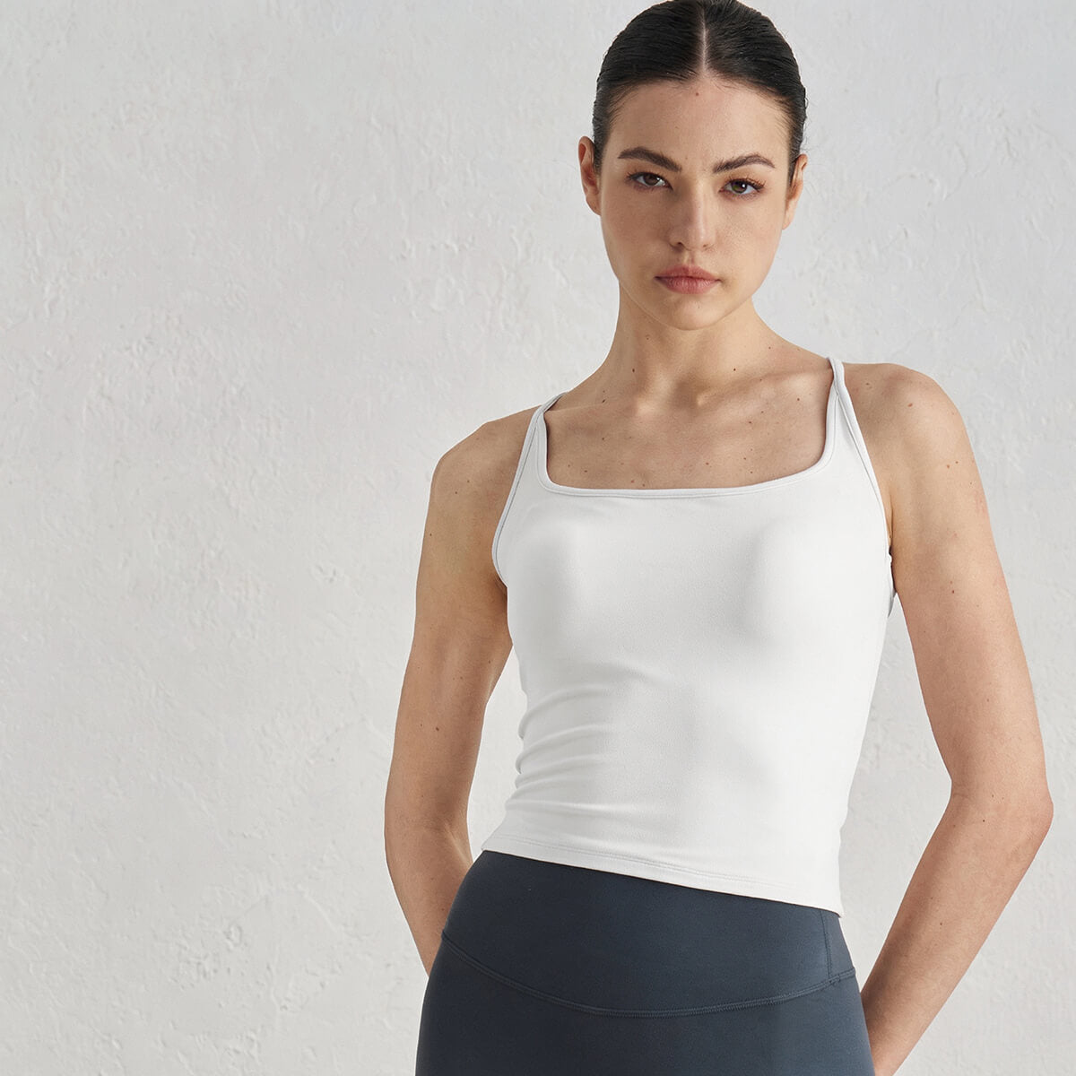 Front view of a woman wearing a white square-neck padded yoga tank top and charcoal leggings.
