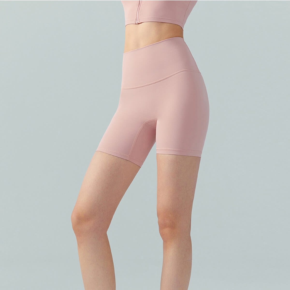 Front view of a woman wearing dusty pink high-waisted biker shorts designed for yoga and gym workouts.