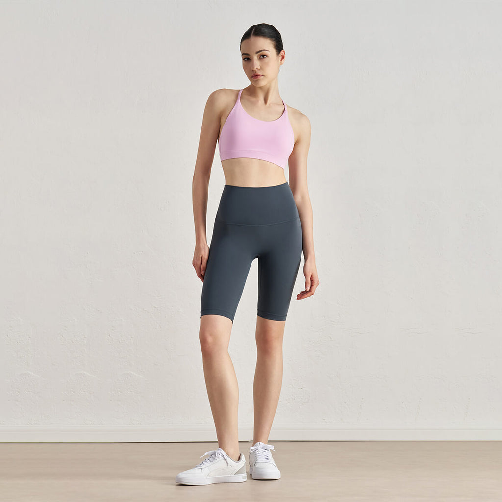Full-body view of a model in deep grey athletic shorts and a light pink sports bra with sneakers