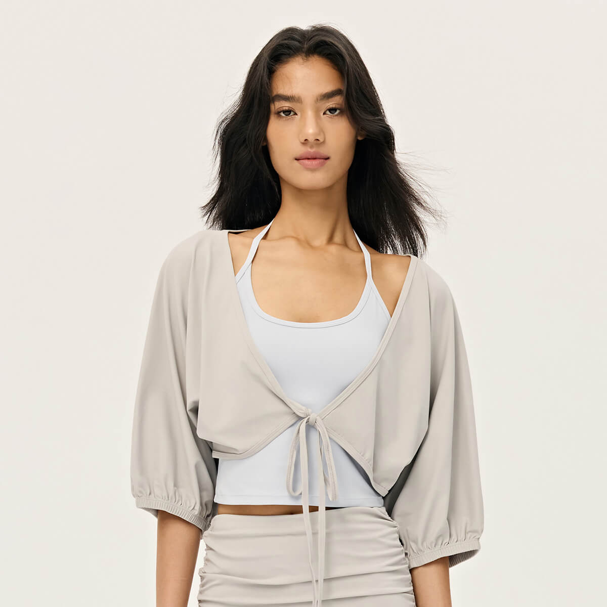 Front view of a woman wearing a light grey tie-front cropped shrug with balloon sleeves over a white halter top.