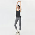 Full front view of a woman wearing a black scoop neck activewear tank top and grey leggings for a gym session.