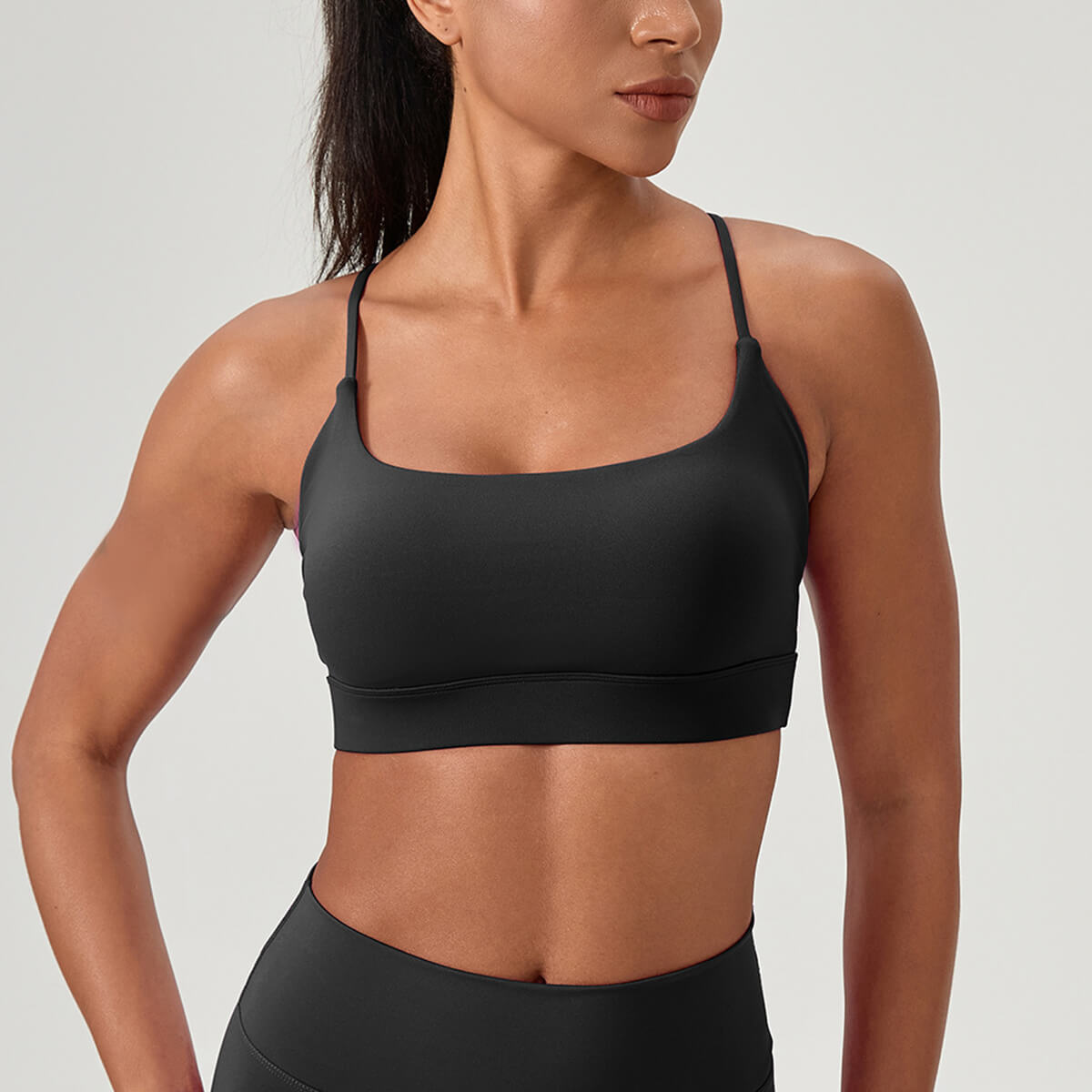 Front view of a woman wearing a classic black scoop-neck sports bra with spaghetti straps, ideal for yoga and Pilates.