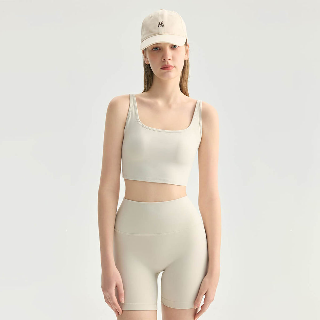 Front view of a woman in a cream-colored square neck yoga crop tank top and matching high-waisted shorts.