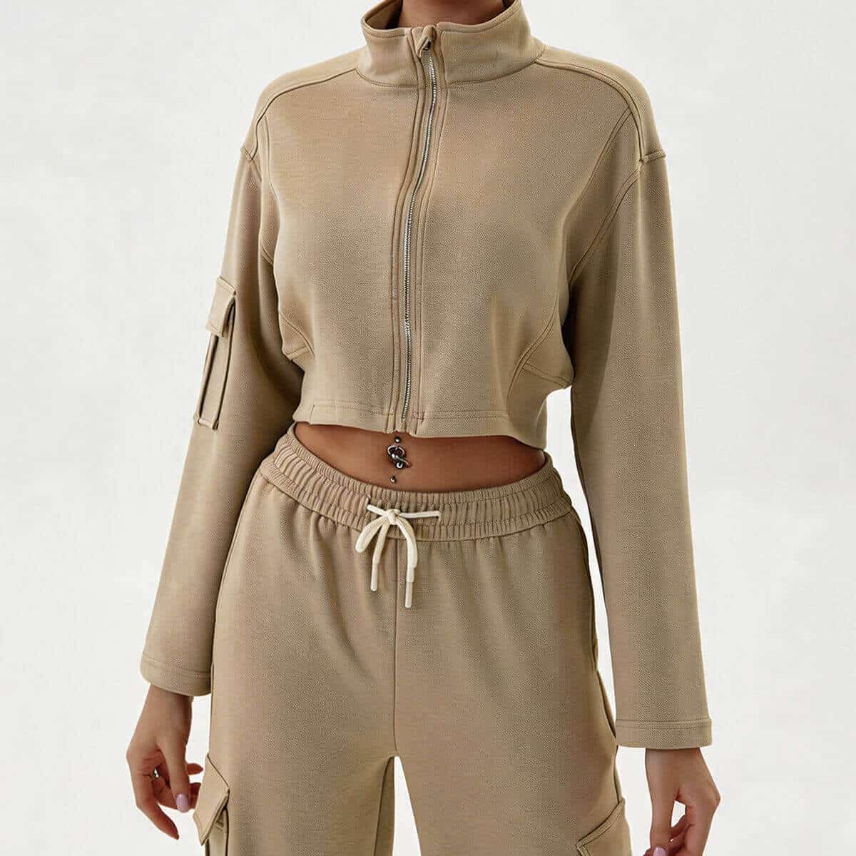 A woman wearing a two-piece khaki athleisure set consisting of a cropped full-zip mock neck jacket with a utility sleeve pocket and matching high-waisted cargo joggers with a drawstring waist.