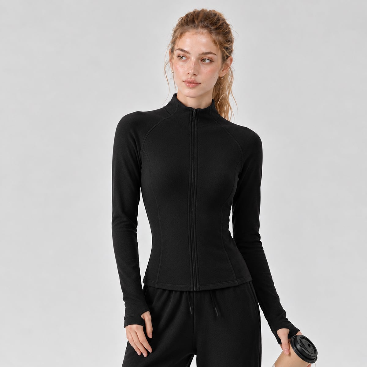 Woman holding a coffee cup in a black slim-fit thermal track jacket.