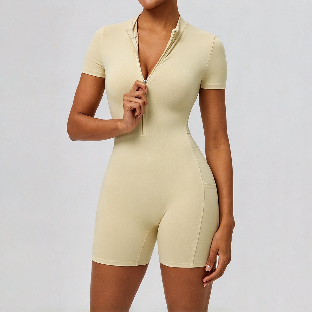 Model unzipping a butter yellow short-sleeve workout romper at the collar.
