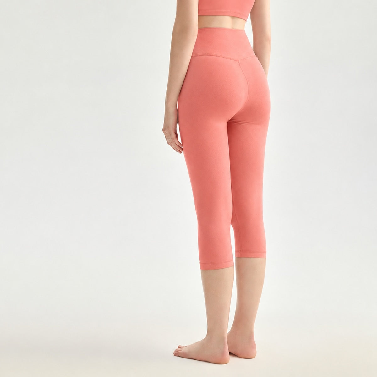 Back view of a woman wearing terracotta high-waisted capri yoga leggings.