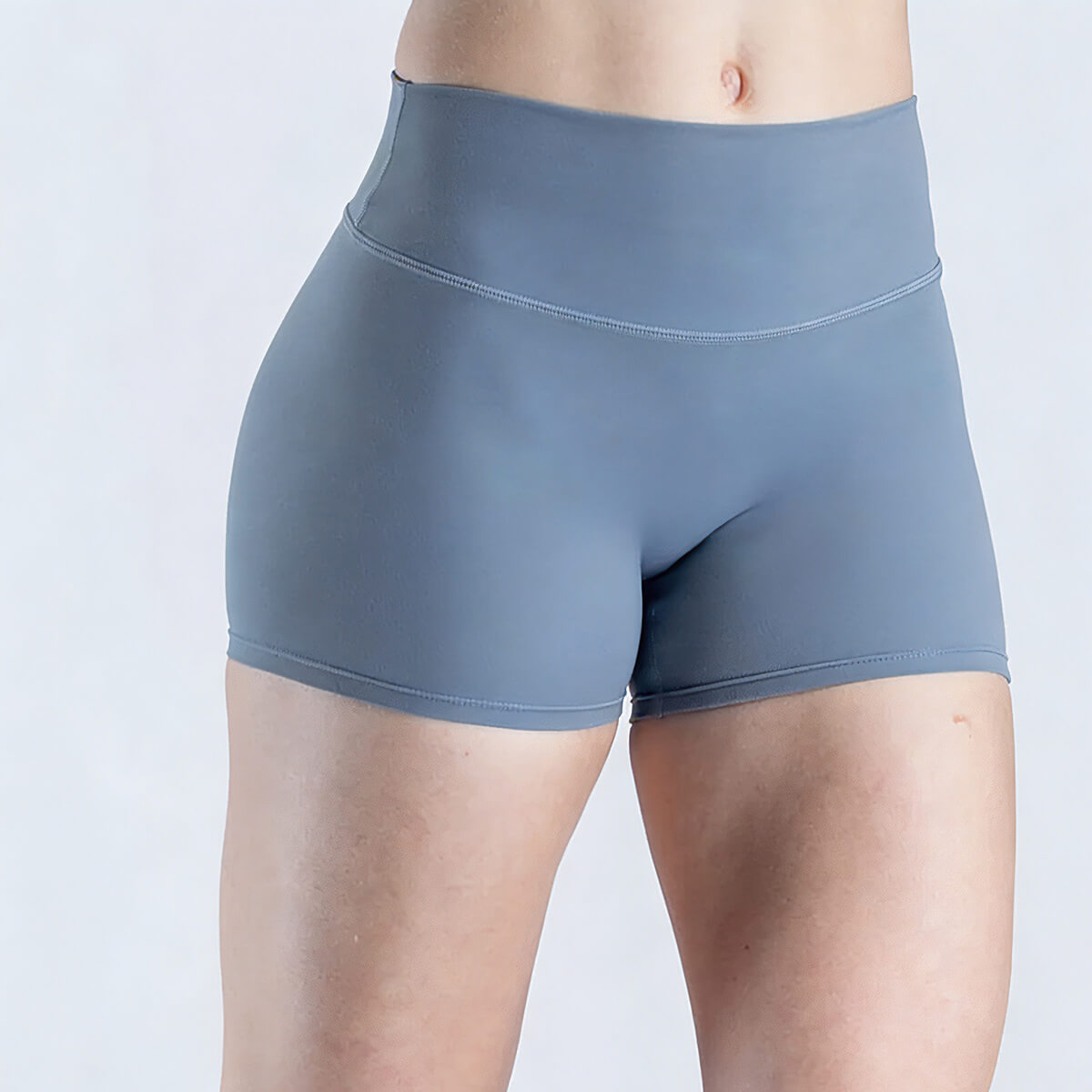 Front view of a woman wearing slate blue high-waisted yoga shorts with a wide tummy-control waistband.