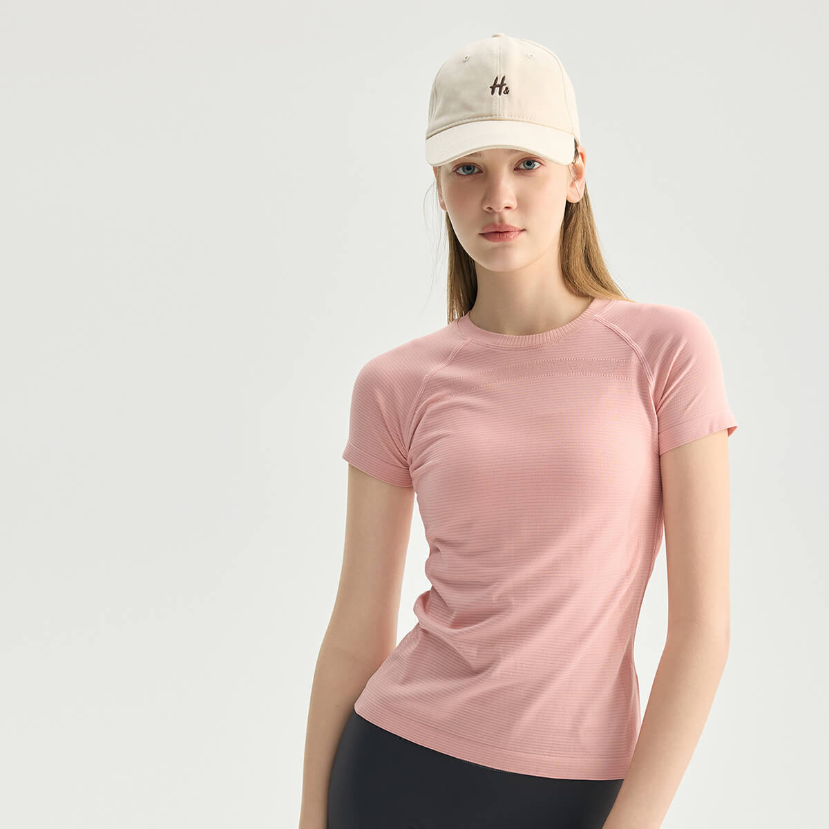 A woman in a blush pink moisture-wicking gym shirt paired with a neutral baseball cap.