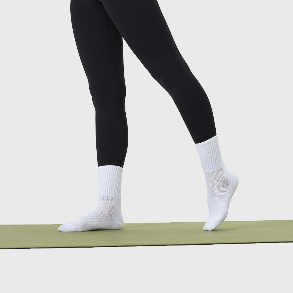Women's non-slip grip pilates yoga socks standing on yoga mat in white with custom logo, athletic apparel manufacturer.
