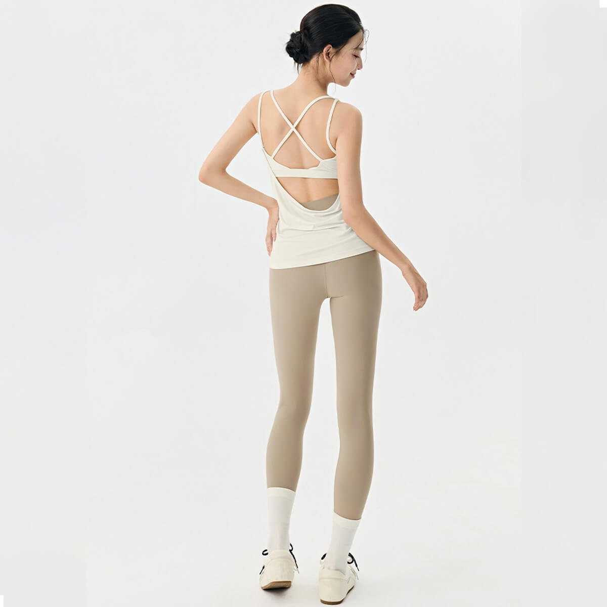 Full back view of a woman wearing a cream 2-in-1 open back yoga tank top and khaki leggings.