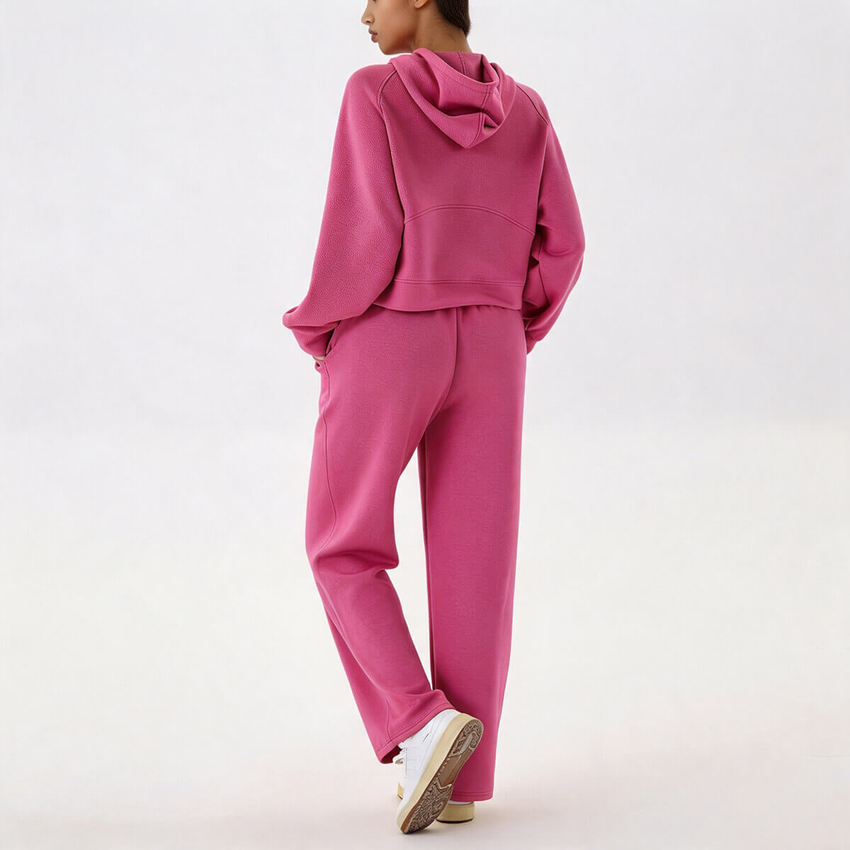 Full back view of a woman wearing a hot pink cropped hoodie and straight-leg sweatpants set with white sneakers.