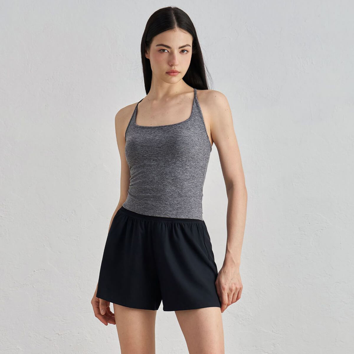 A woman wearing a slim-fit heather gray racerback yoga tank top with black athletic shorts.