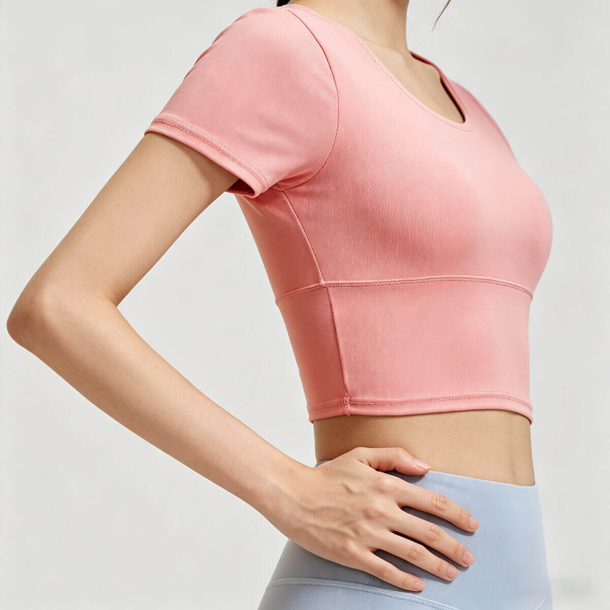 Side view of a women's peach pink short sleeve fitness crop top featuring a wide, stay-put hem for high-intensity gym workouts.
