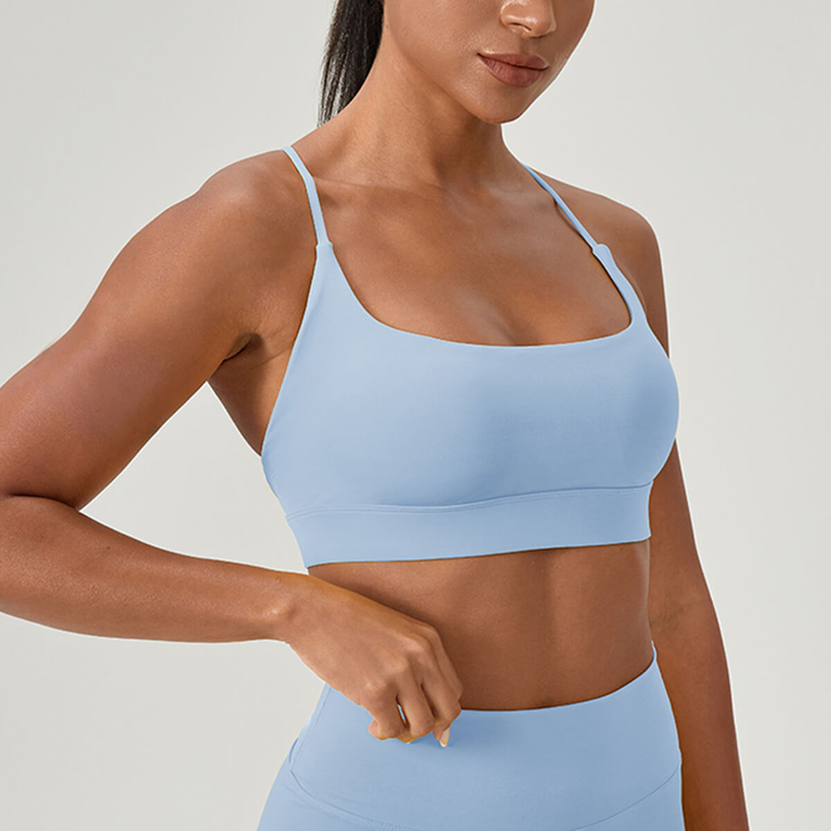 A woman posing in a sky blue strappy athletic bra featuring a smooth, second-skin fabric finish.