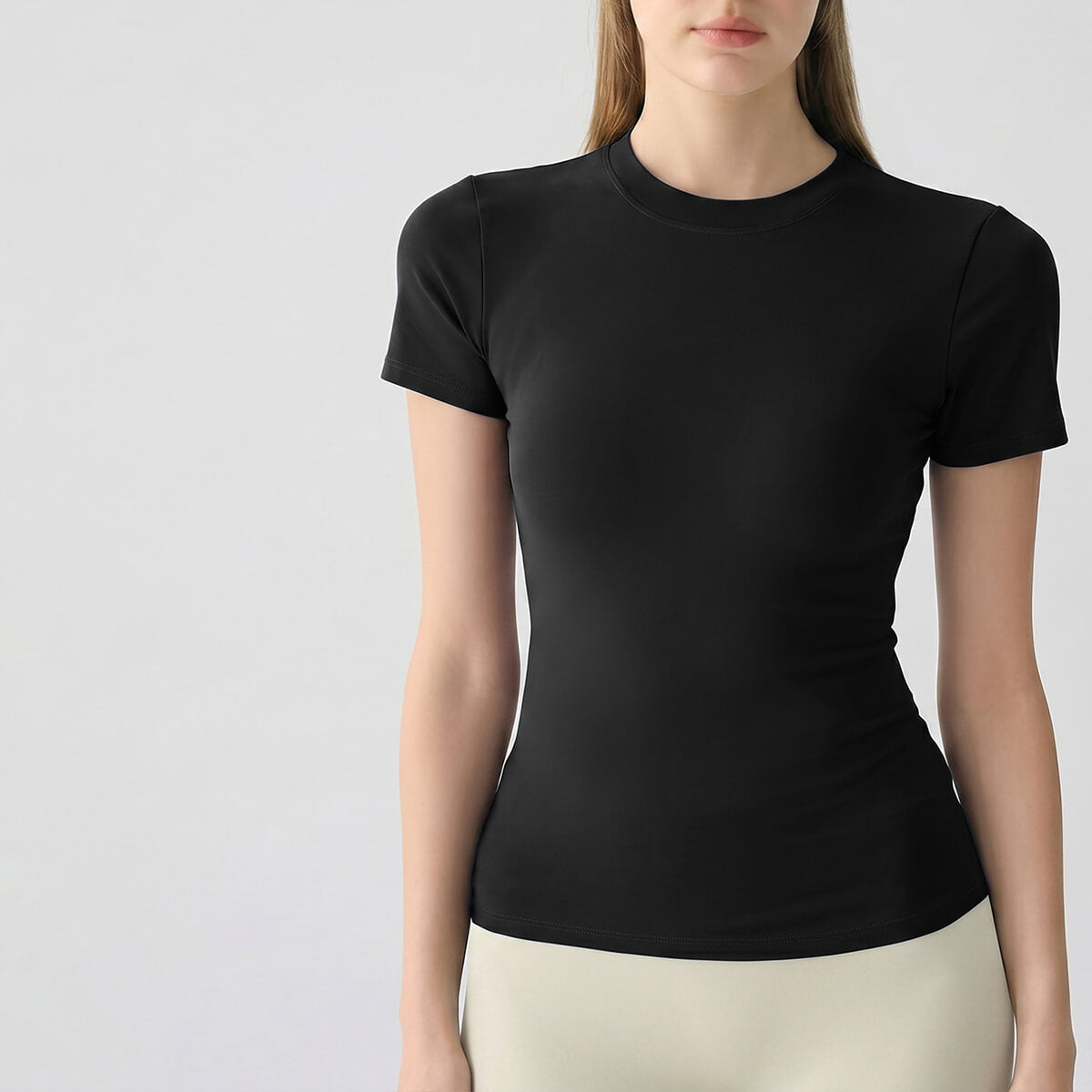 Front view of a woman wearing a black slim-fit short-sleeve athletic t-shirt with beige leggings.