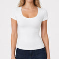 A woman wearing a crisp white slim-fit short sleeve t-shirt with a flattering scoop neck, paired with dark blue denim jeans.