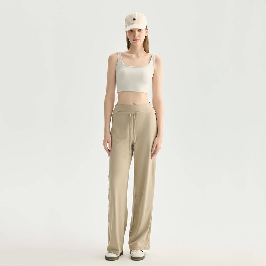 Full body front view of a woman wearing a cream square neck crop tank top and khaki wide-leg yoga pants with a baseball cap for an athleisure look.
