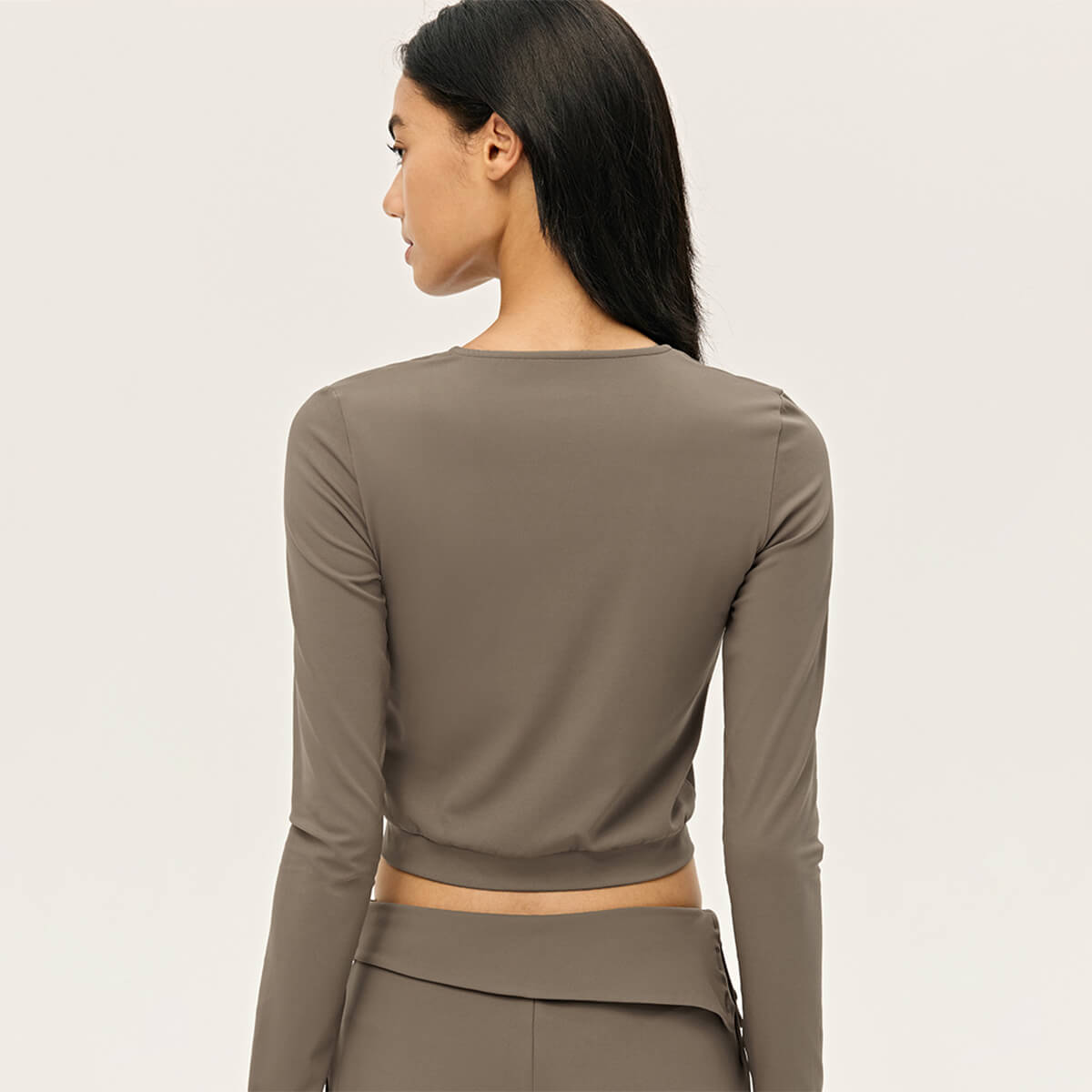 Rear view of a woman in a taupe long sleeve workout zip-up top showcasing the sleek back design.