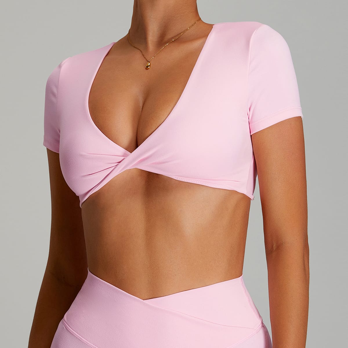 Close-up of the deep V-neck twist-knot detail on a pink short-sleeve sports bra.
