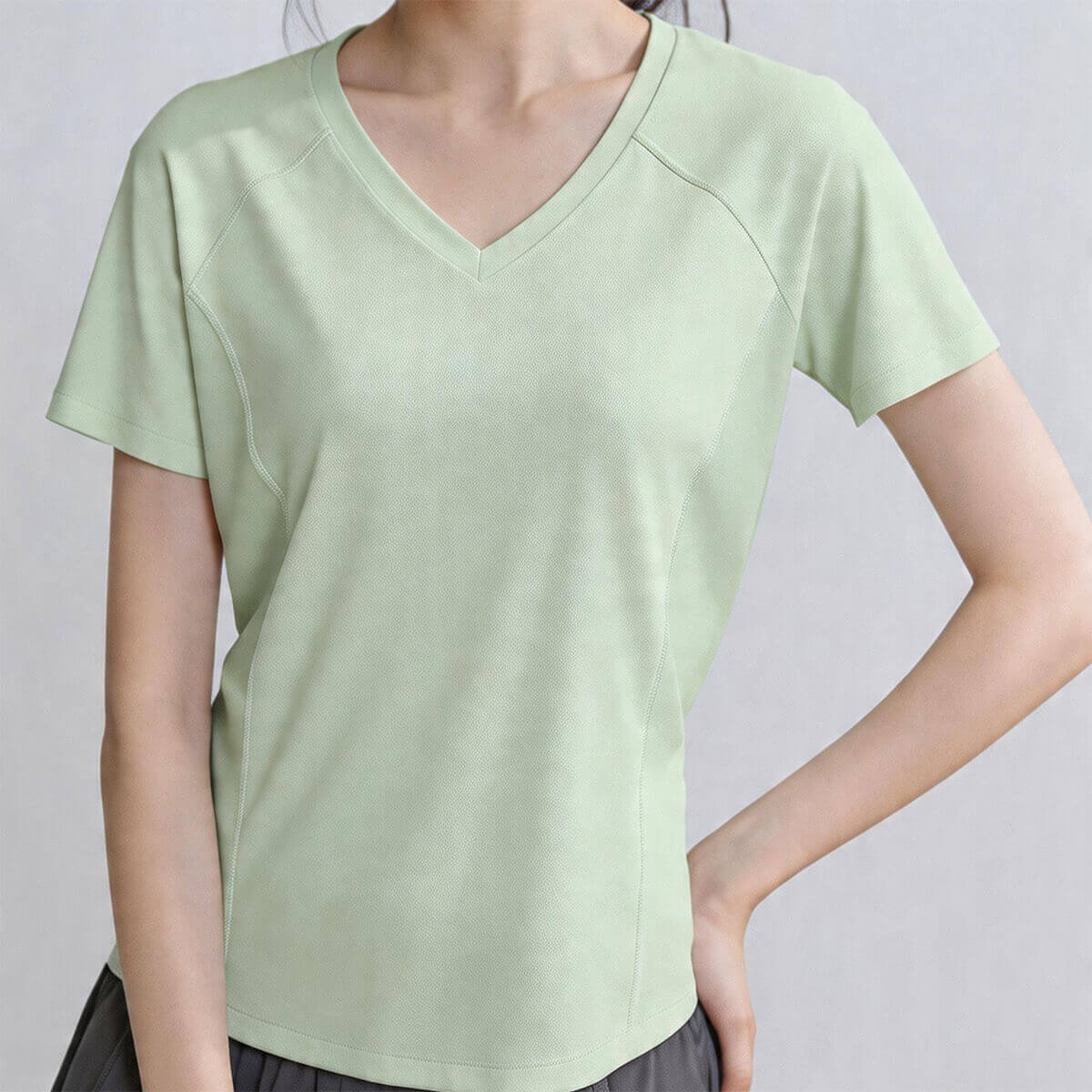 A woman wearing a mint green V-neck breathable athletic shirt featuring moisture-wicking fabric and side mesh panels for summer workouts
