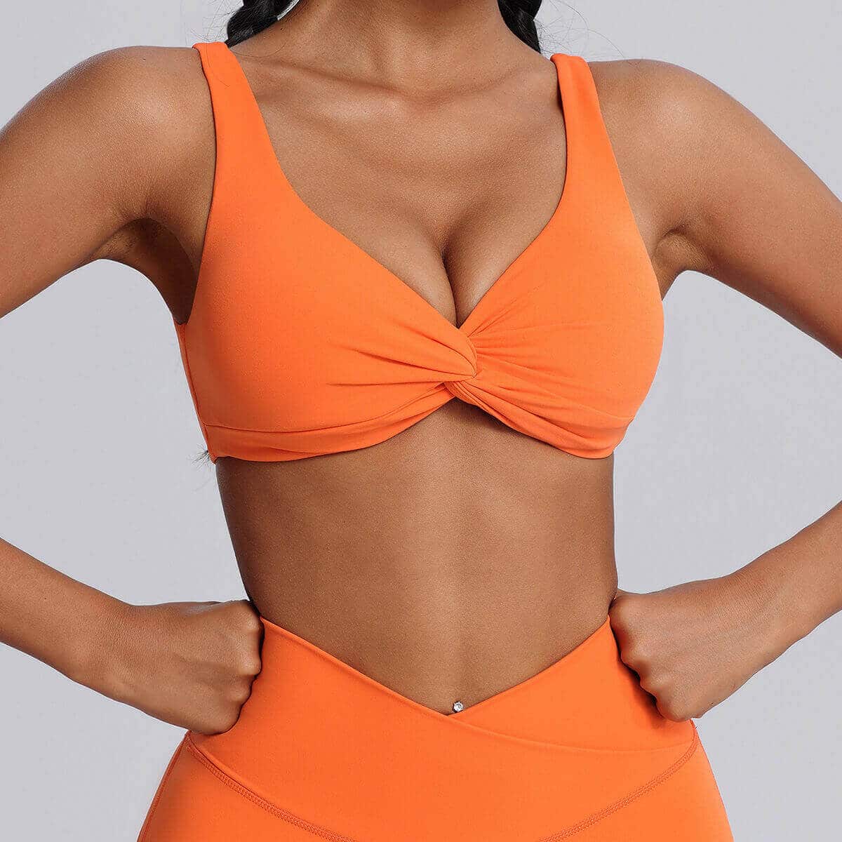 Front view of a vibrant orange twist-front athletic sports bra.
