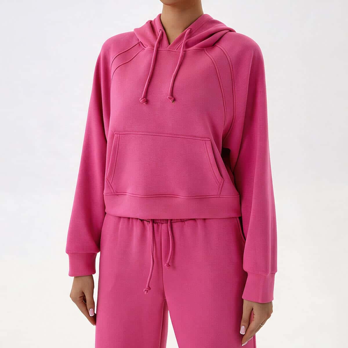 Full front view of a woman wearing a vibrant pink two-piece cropped tracksuit set with a modern, relaxed fit.
