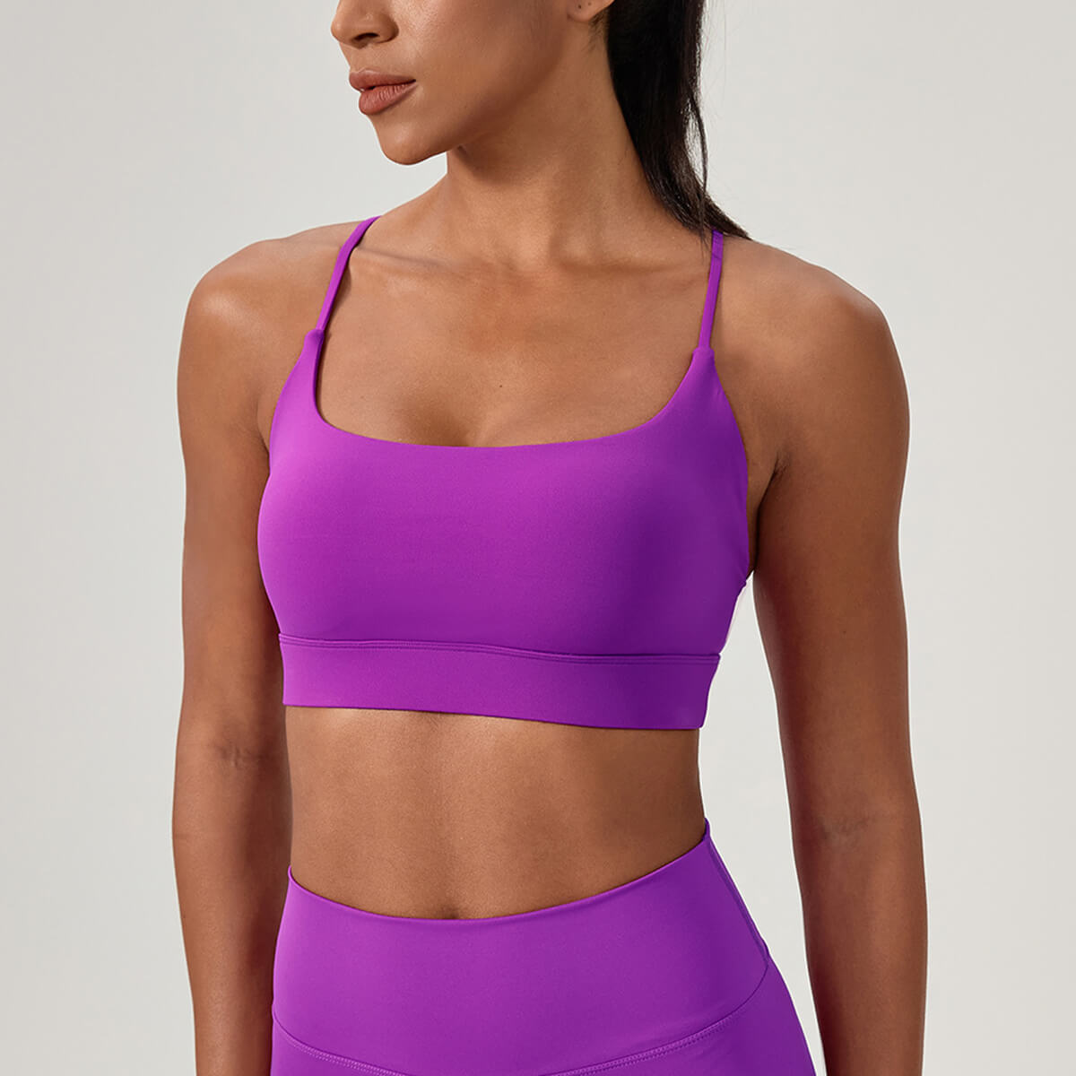 A woman wearing a vibrant purple yoga sports bra with a flattering scoop neckline and sleek thin straps.
