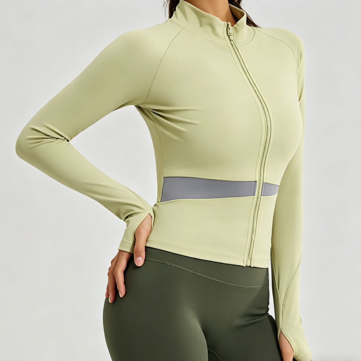 Close-up of a sage green workout zip-up jacket showing functional thumbholes and the flattering waist-contouring mesh design