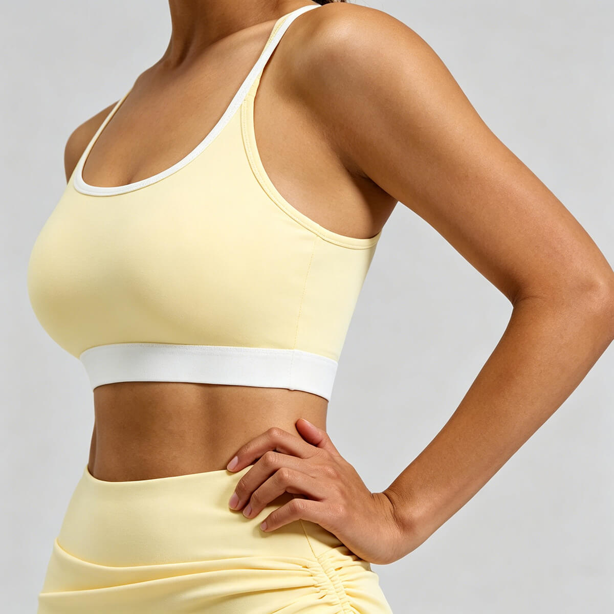 Side profile of a women's pale yellow strappy sports bra showing the seamless fit and contrasting white elastic band for a stylish athletic look